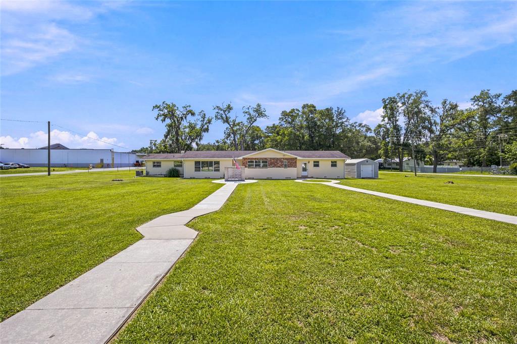 A single-story house with a brick facade stands behind a large lawn and concrete walkways — 110 NE 5TH STREET, WILLISTON, FL