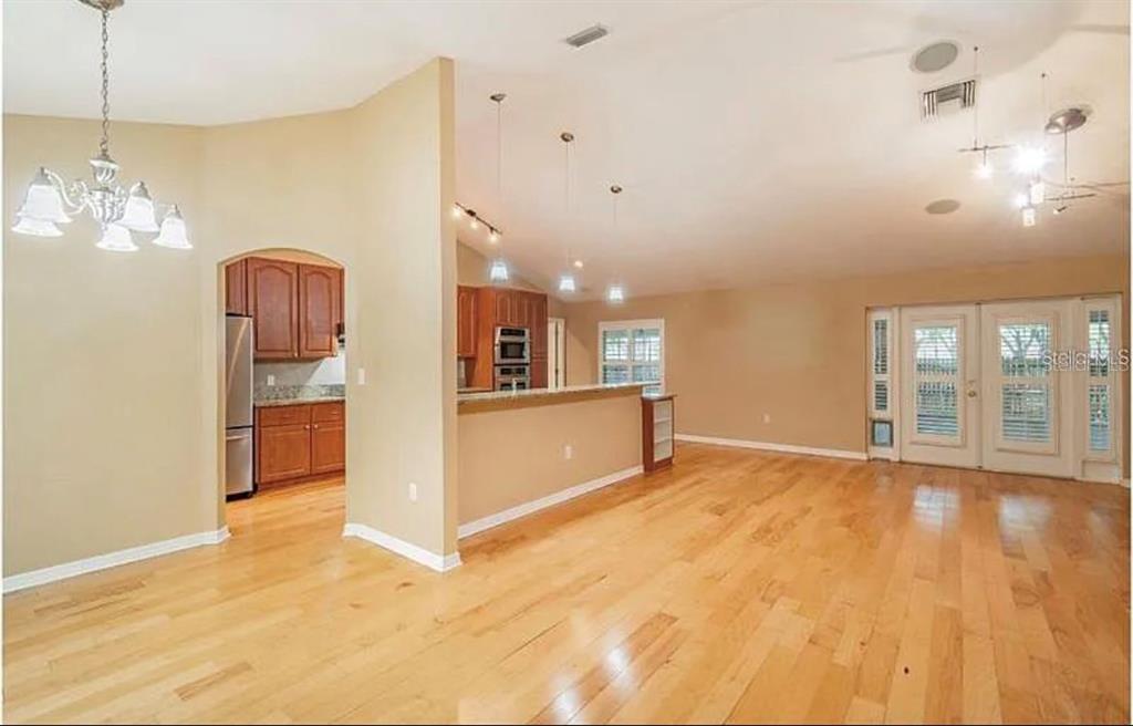 An open-concept living area features light hardwood floors, a kitchen with wood cabinets, and pendant lighting — 4914 N MENDENHALL DRIVE, TAMPA, FL