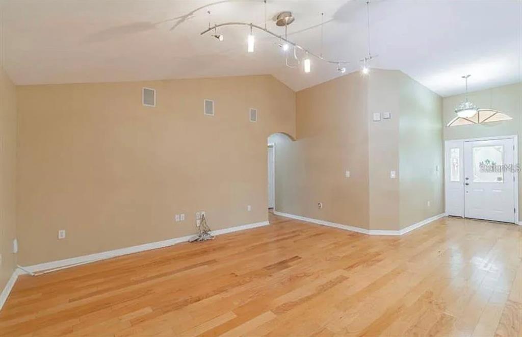 An empty living room features hardwood floors, vaulted ceilings, and a modern track lighting fixture — 4914 N MENDENHALL DRIVE, TAMPA, FL