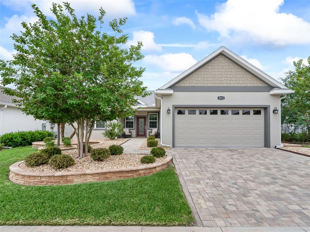 A single-story house features a paved driveway, a stone-walled garden bed, and a large tree — 5015 NE 125TH LOOP, OXFORD, FL