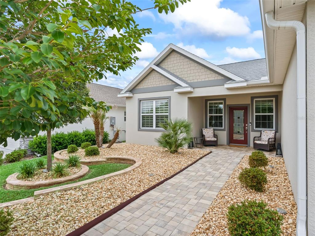 A single-story house exterior features a paved walkway, rock landscaping, and a red front door — 5015 NE 125TH LOOP, OXFORD, FL