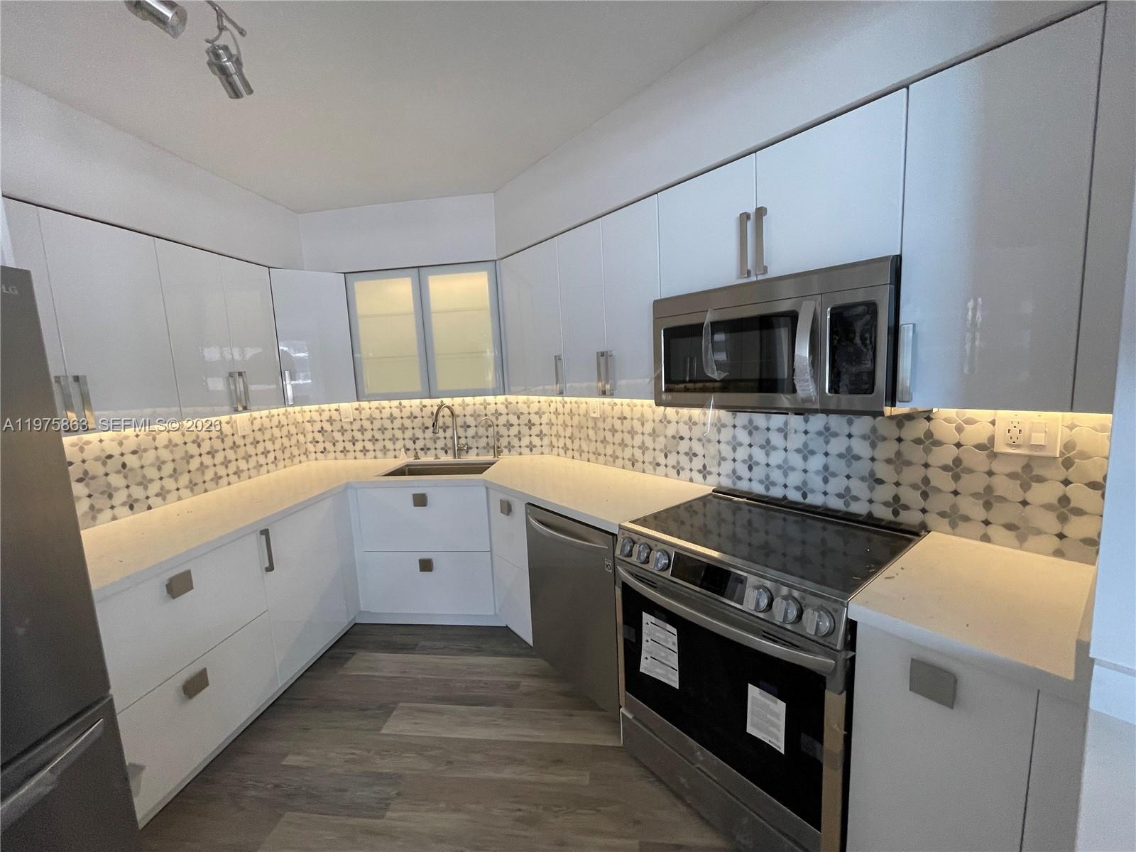 A modern kitchen features white glossy cabinets, stainless steel appliances, and a patterned tile backsplash — 5161 Collins Ave # 1012, Miami Beach FL 33140, MIAMI BEACH, FL