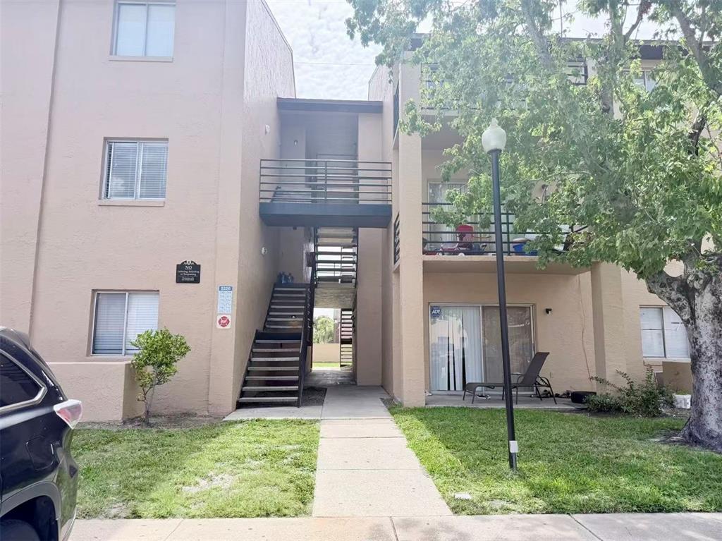 A three-story apartment building exterior features an open-air staircase and a concrete walkway — 5226 VIA HACIENDA CIRCLE UNIT A214, ORLANDO, FL