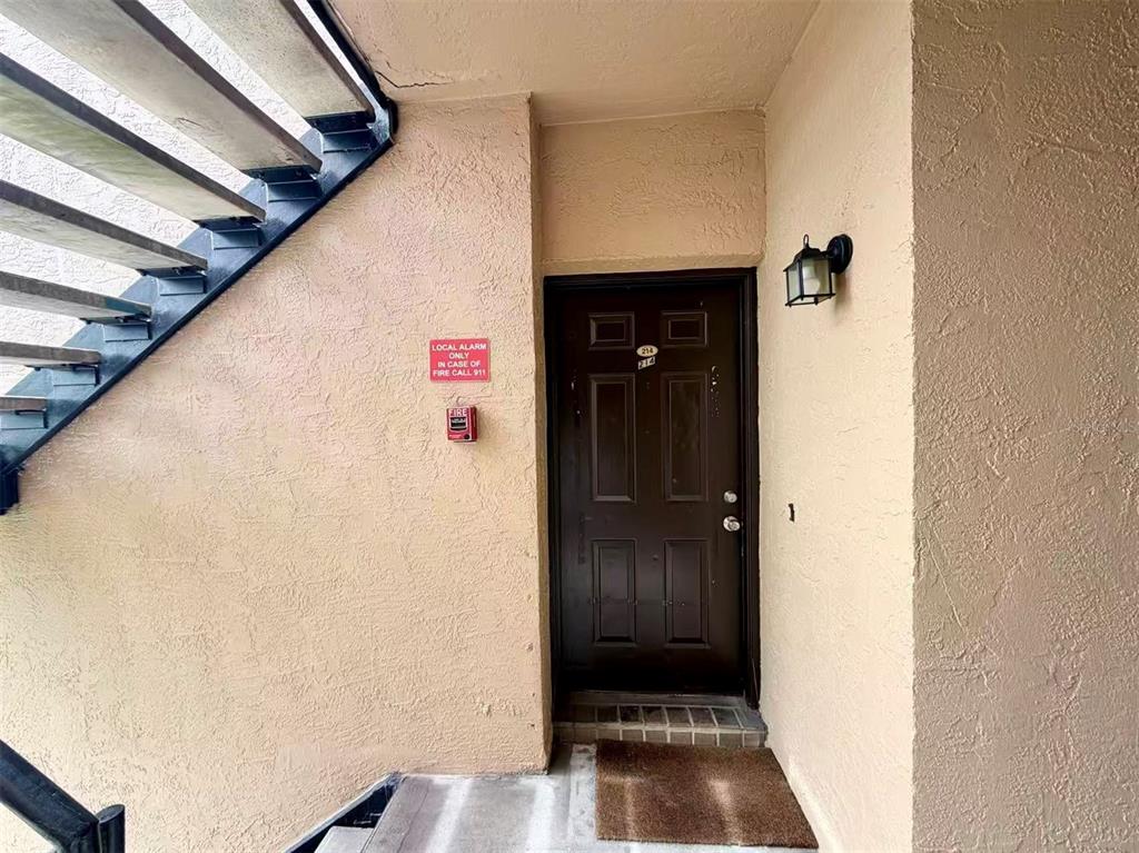 An exterior view of a brown apartment door with a fire alarm and staircase — 5226 VIA HACIENDA CIRCLE UNIT A214, ORLANDO, FL