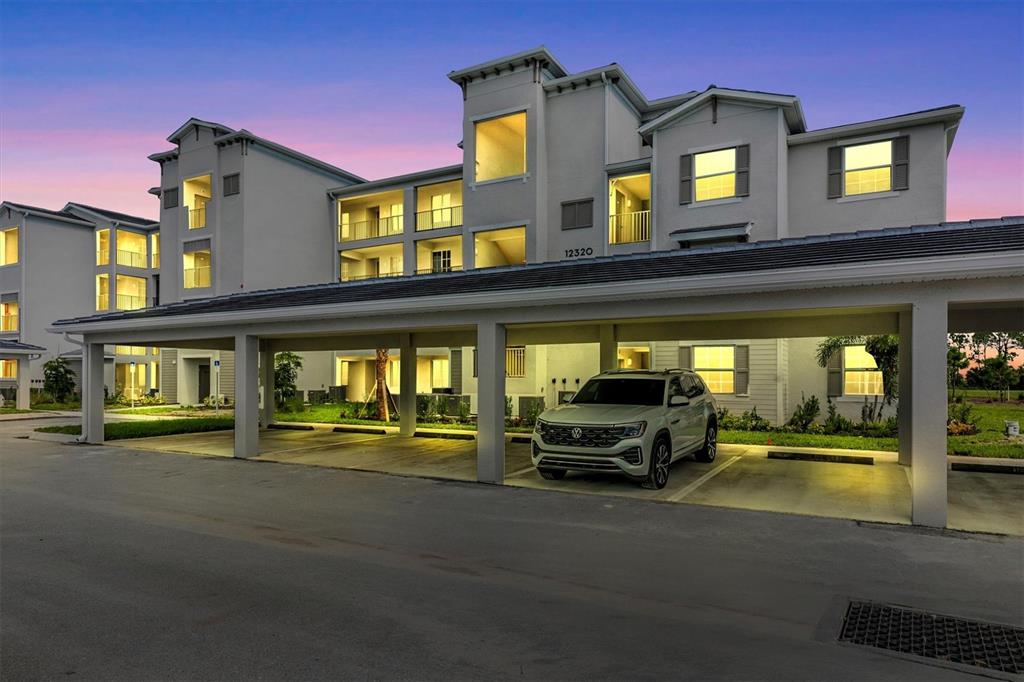 A multi-story apartment building exterior features a covered parking area with a parked SUV — 12320 WELLEN GOLF STREET UNIT 403, VENICE, FL