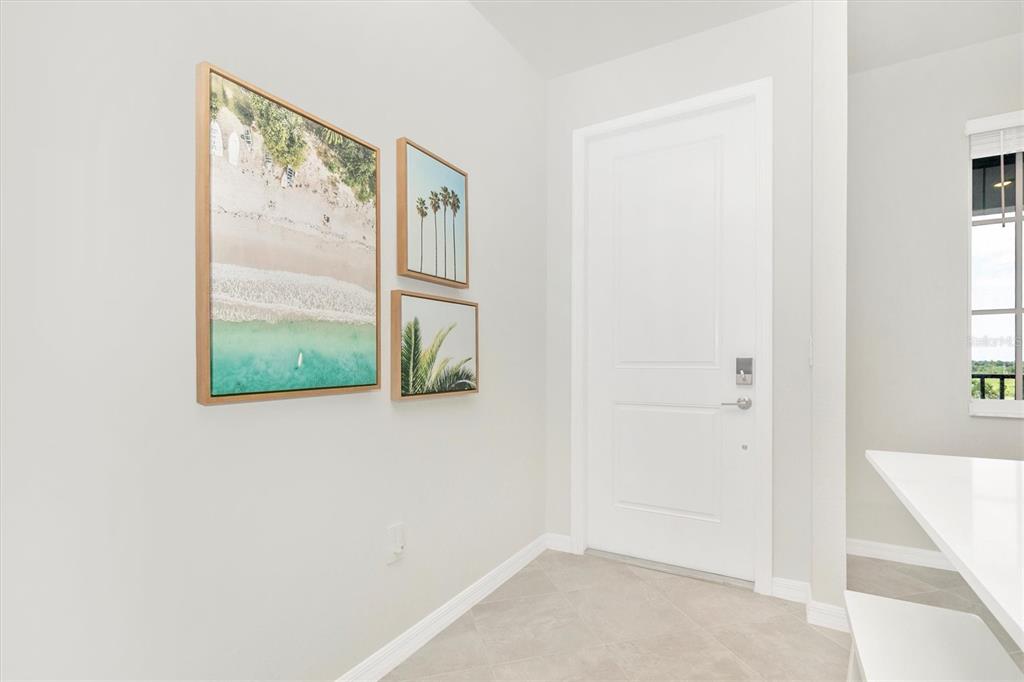 A bright entryway features light tile flooring, a white door, and three framed tropical wall prints — 12320 WELLEN GOLF STREET UNIT 403, VENICE, FL