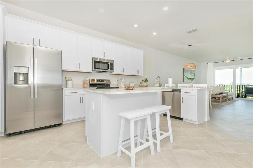 A modern kitchen features white cabinetry, stainless steel appliances, a central island, and tile flooring — 12320 WELLEN GOLF STREET UNIT 403, VENICE, FL