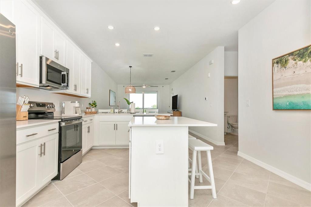 A modern kitchen features white cabinets, stainless steel appliances, and a central island with seating — 12320 WELLEN GOLF STREET UNIT 403, VENICE, FL