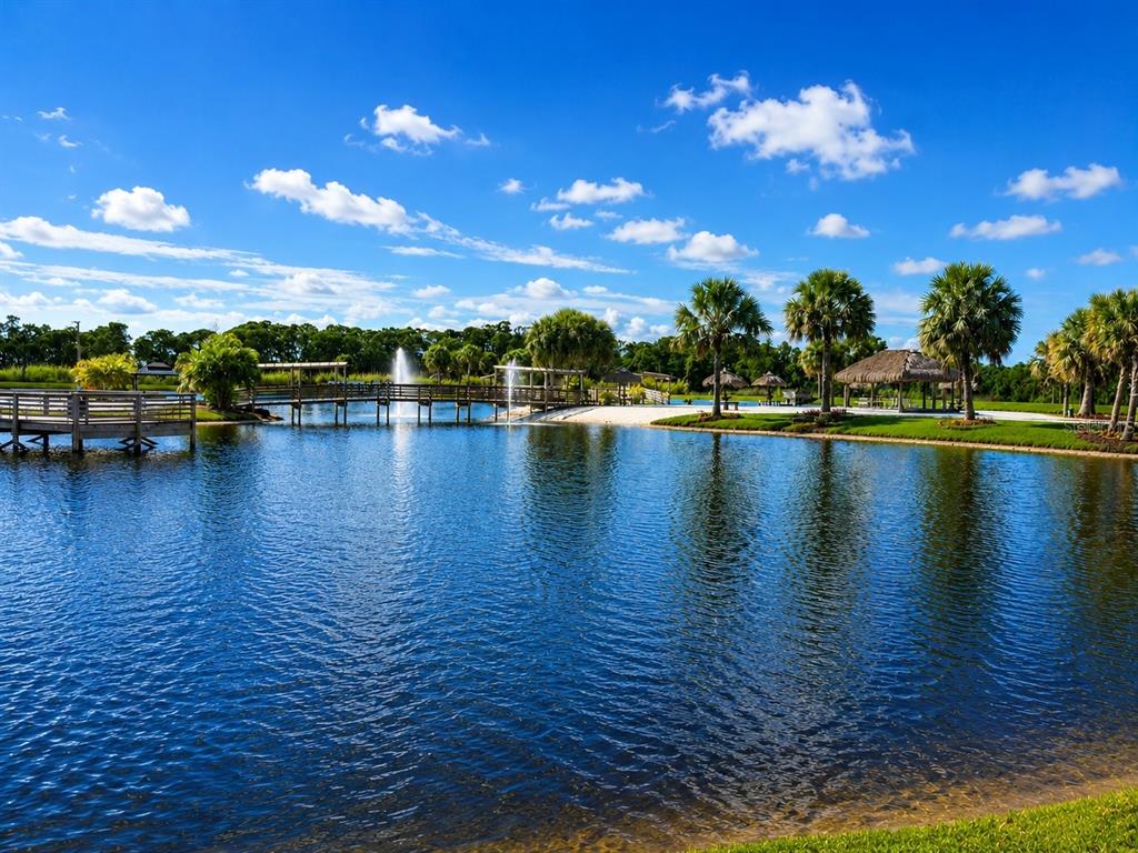 A wooden bridge crosses a lake with a fountain, palm trees, and a thatched-roof pavilion — 0 CR-630 E Lot 108, LAKE WALES, FL