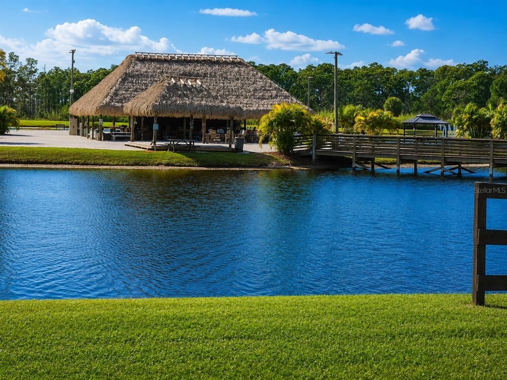 A thatched-roof tiki hut sits beside a pond with a wooden bridge in the foreground — 0 CR-630 E Lot 108, LAKE WALES, FL