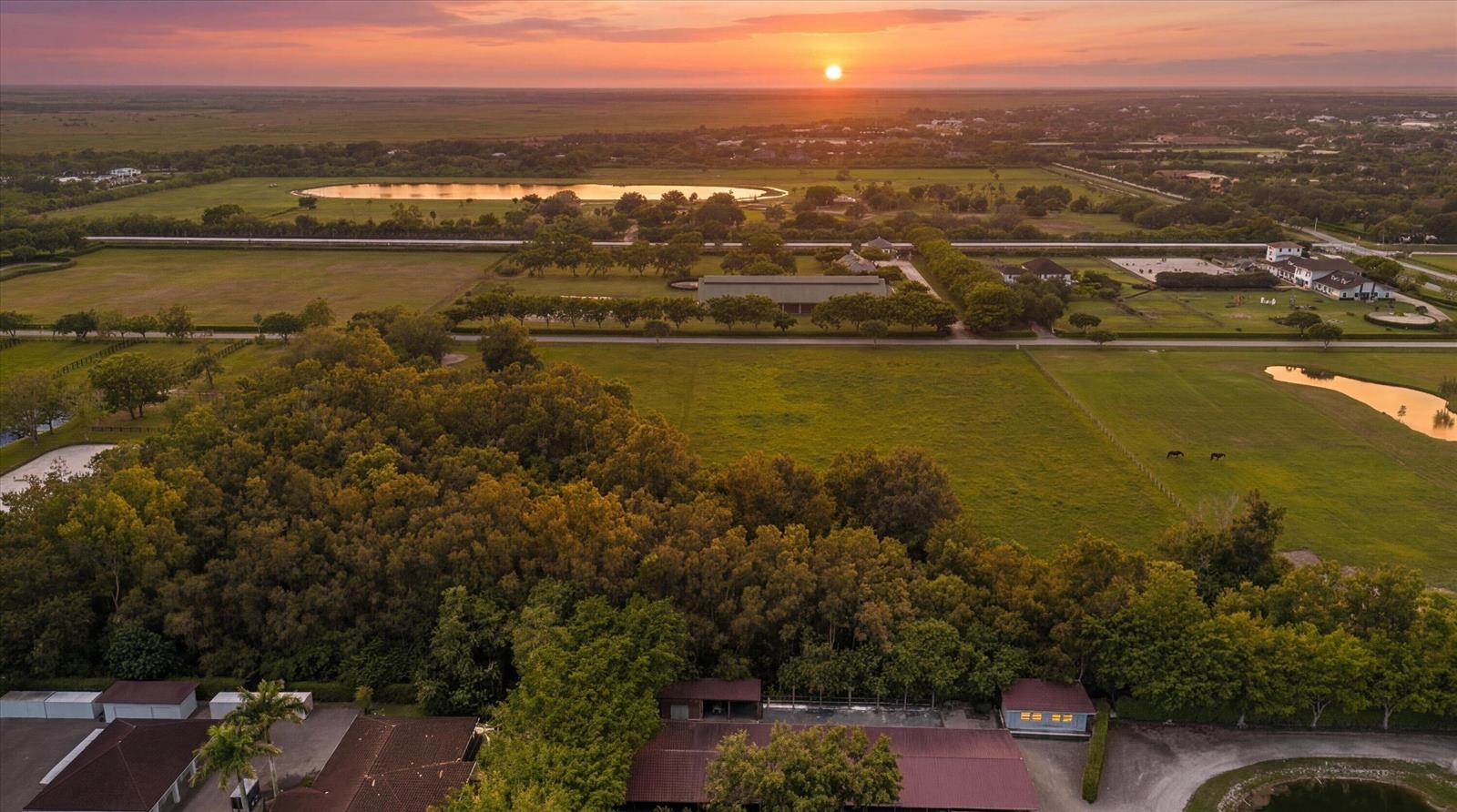 An aerial view of a rural property featuring pastures, trees, and buildings at sunset — 5266 138th Terrace S, Wellington FL 33449, WELLINGTON, FL
