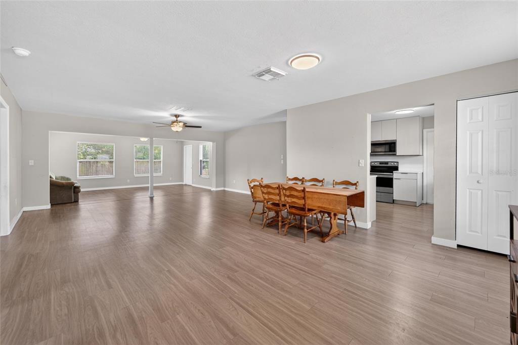 An open-concept living and dining area with light wood-look flooring and a kitchen beyond — 7156 LOCKWOOD STREET, SPRING HILL, FL