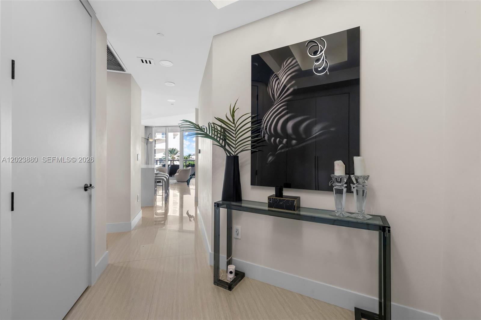 A hallway features a glass console table, abstract wall art, and light-colored tile flooring — 100 S Pointe Dr # 509, Miami Beach FL 33139, MIAMI BEACH, FL