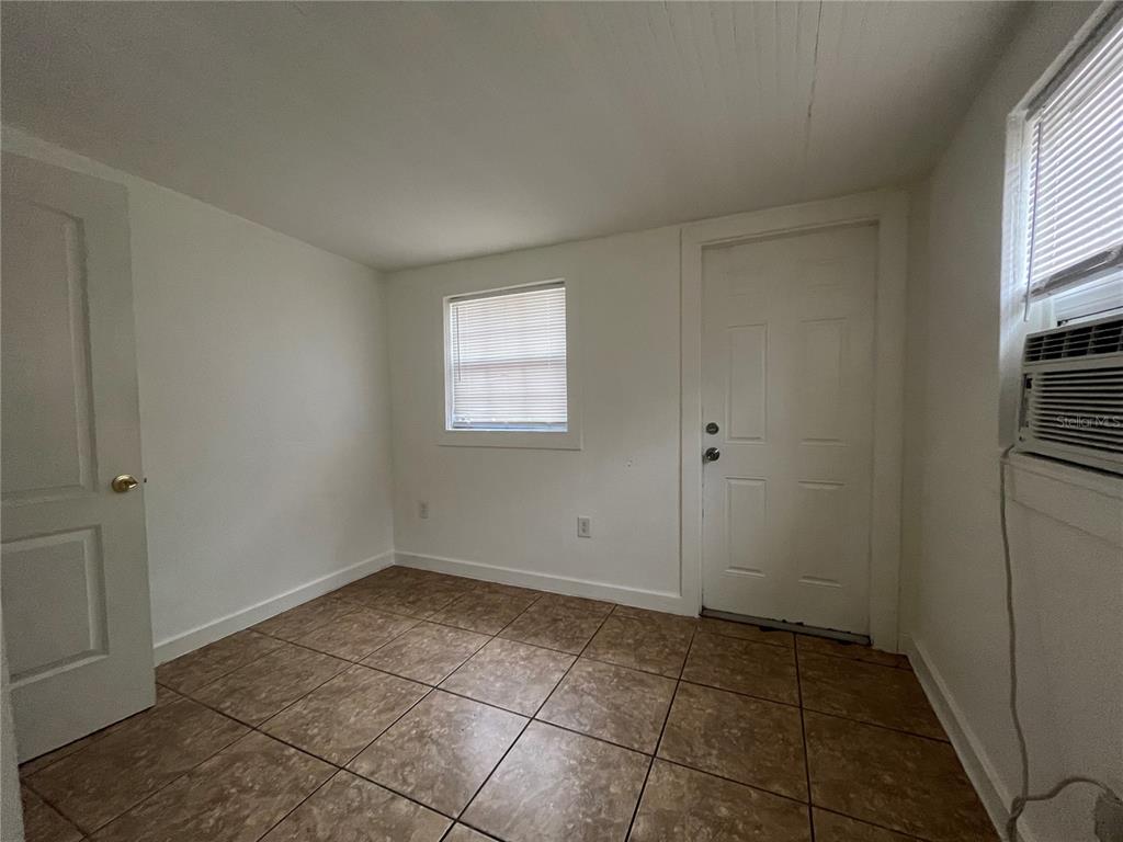An empty room features white walls, tan tile flooring, a window, and a door — 720 22ND AVENUE W, BRADENTON, FL