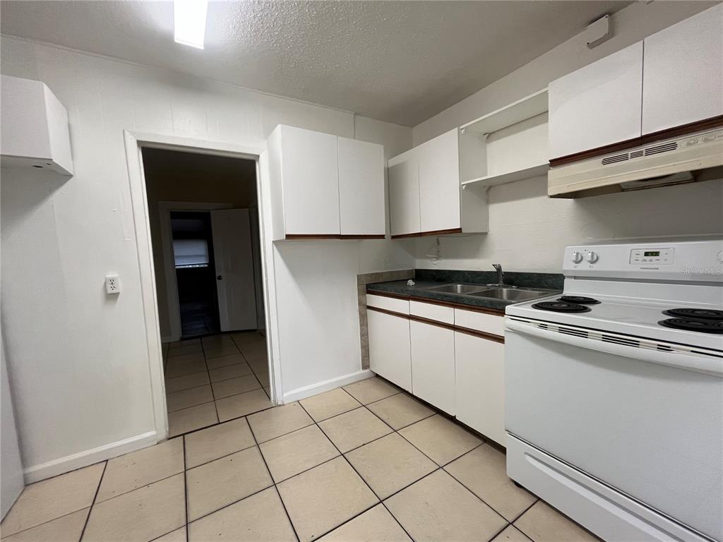 A kitchen features white cabinets, a white stove, a double sink, and tiled flooring — 720 22ND AVENUE W, BRADENTON, FL