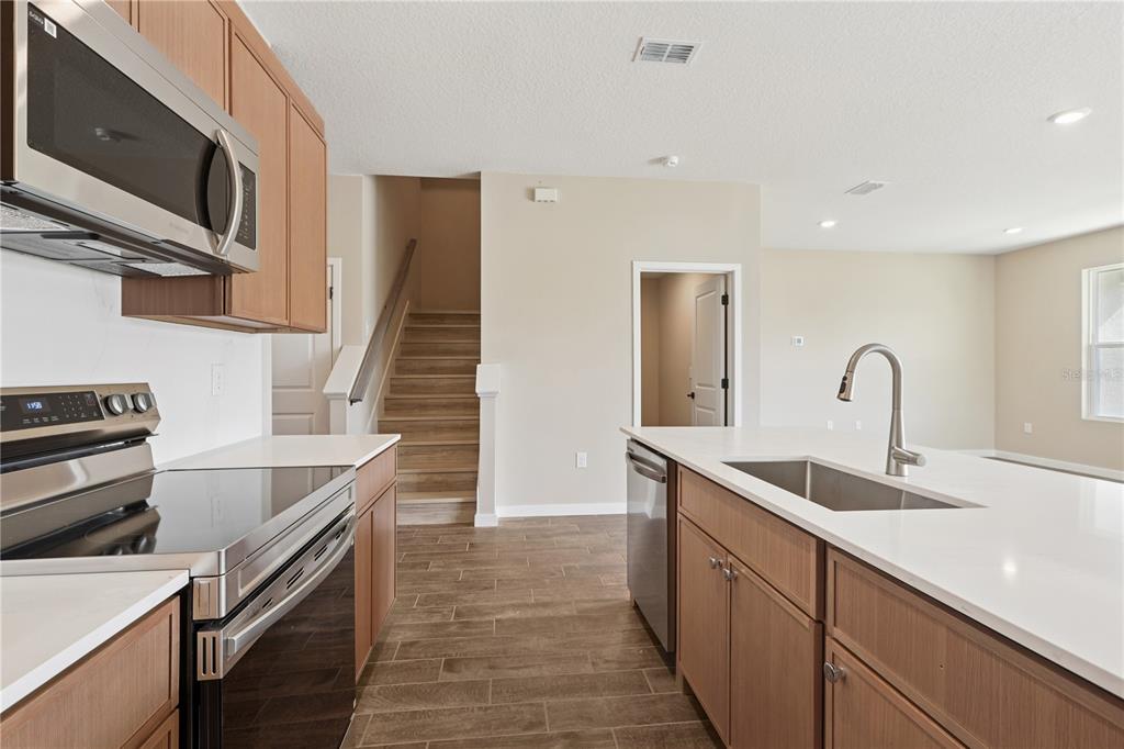 A kitchen with wood cabinets, stainless steel appliances, white countertops, and stairs in the background — 4488 NW 37TH STREET ROAD, OCALA, FL