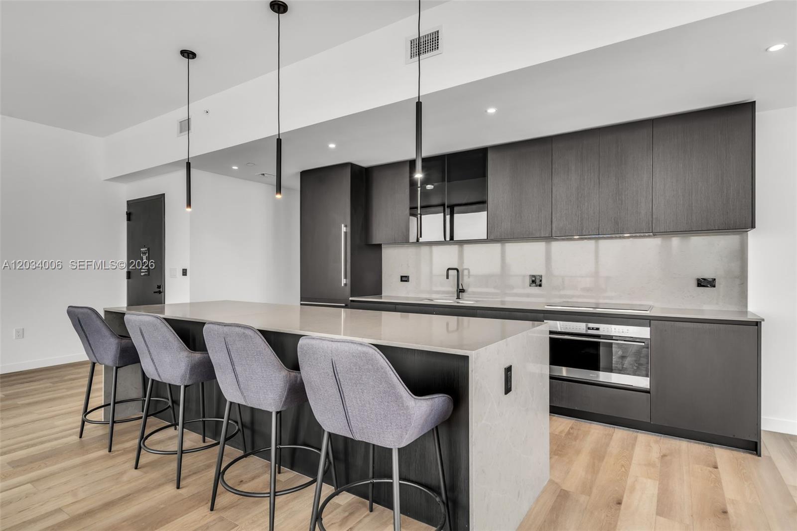 A modern kitchen features dark cabinetry, a stone-topped island with bar stools, and light flooring — 20 NE 11th St # 5102, Miami FL 33132, MIAMI, FL