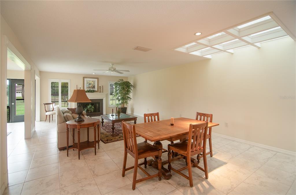 A living and dining area with tile floors, a fireplace, and a large skylight — 7403 CARNOUSTIE DRIVE UNIT 7D, SARASOTA, FL