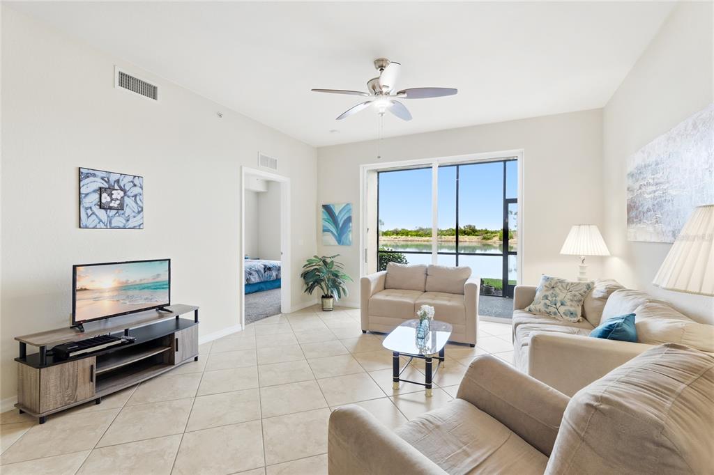 A living room with tile floors, a ceiling fan, and a sliding door to a lake — 7911 GRAND ESTUARY TRAIL UNIT 104, BRADENTON, FL