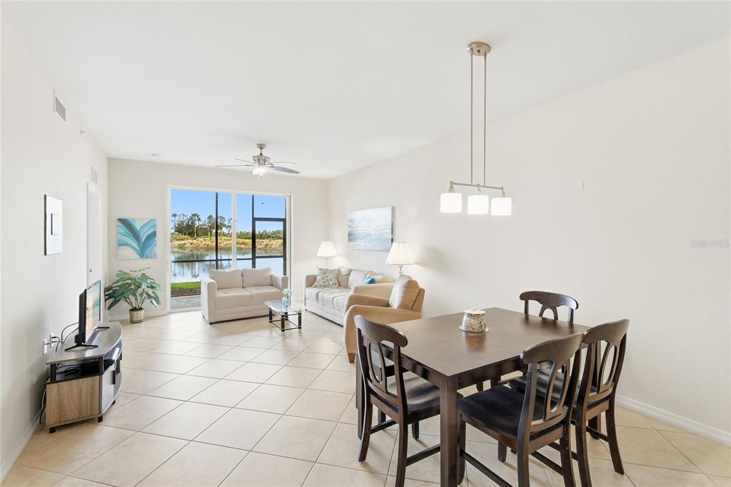 A living and dining area with tile floors, neutral walls, and a view of a lake — 7911 GRAND ESTUARY TRAIL UNIT 104, BRADENTON, FL