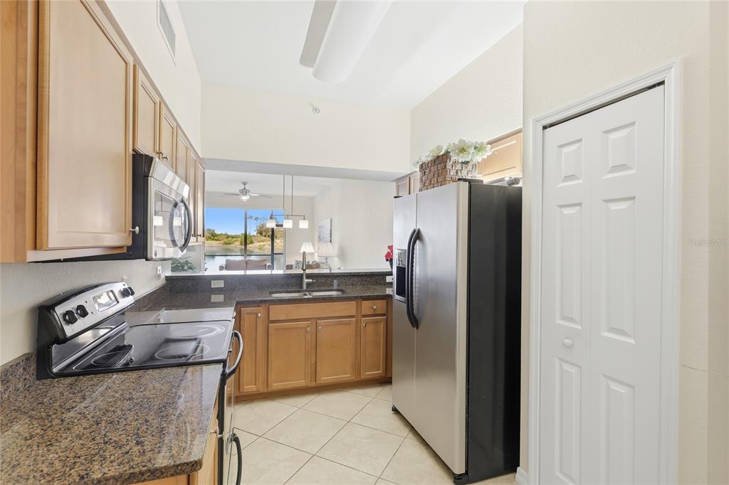 A kitchen with light wood cabinets, granite countertops, stainless steel appliances, and a lake view — 7911 GRAND ESTUARY TRAIL UNIT 104, BRADENTON, FL