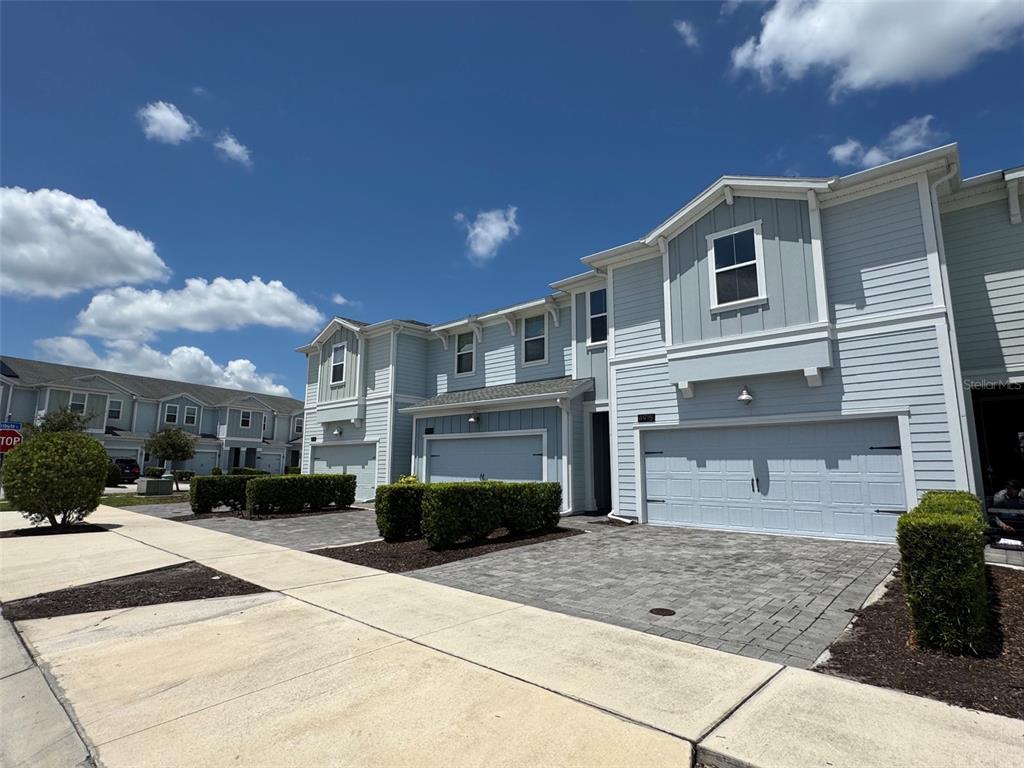 A row of light blue two-story townhouses with paved driveways and manicured hedges — 4915 TRIBUTE TRAIL, KISSIMMEE, FL