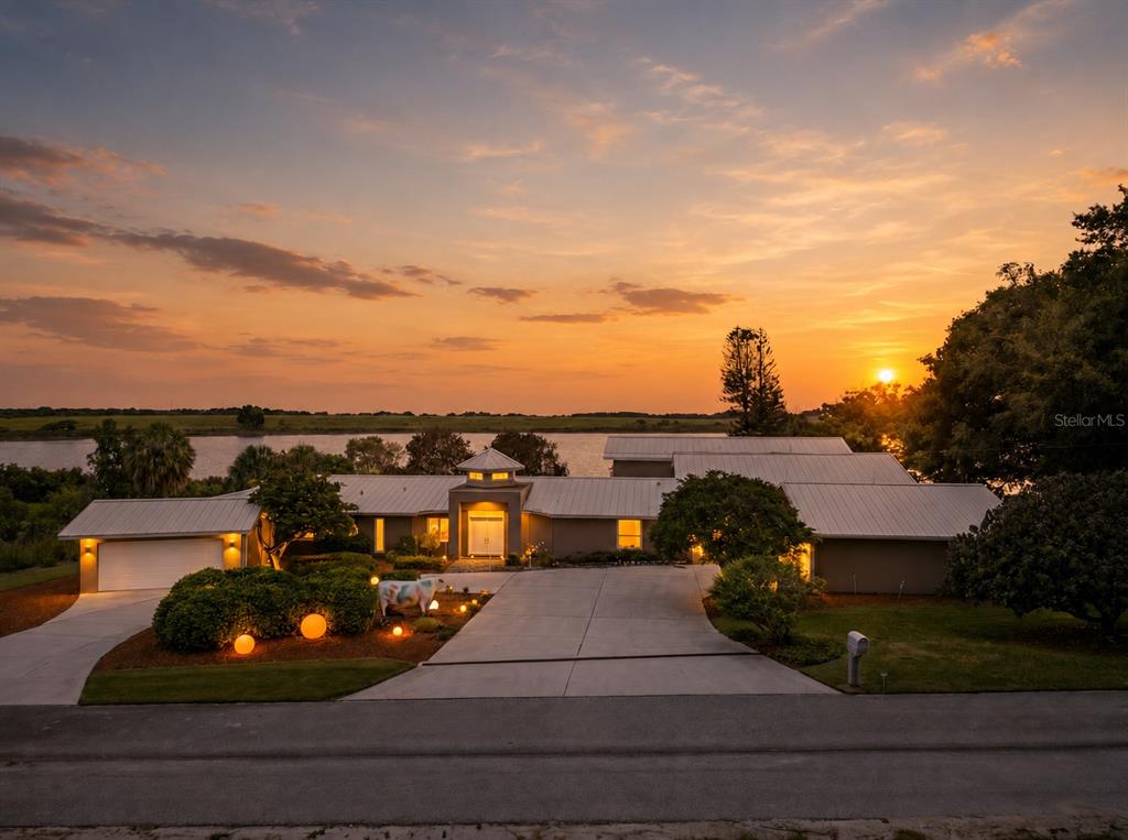 A single-story house with a metal roof and a driveway sits by a lake at sunset — 775 S ILAKEE AVENUE, LAKE ALFRED, FL