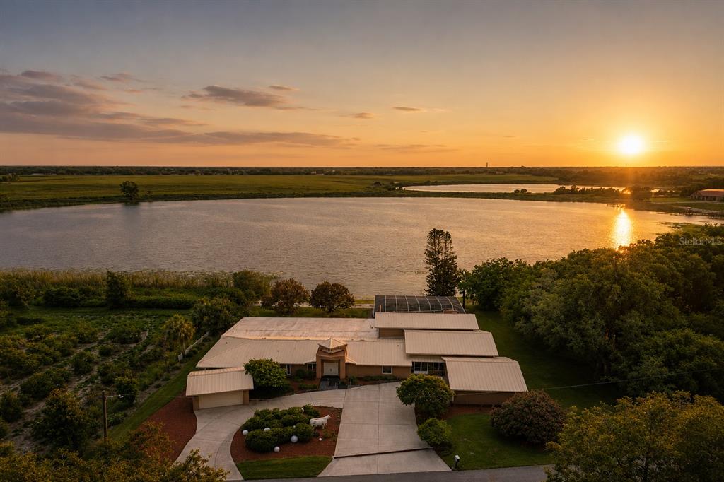 An aerial view of a house with a metal roof beside a lake at sunset — 775 S ILAKEE AVENUE, LAKE ALFRED, FL