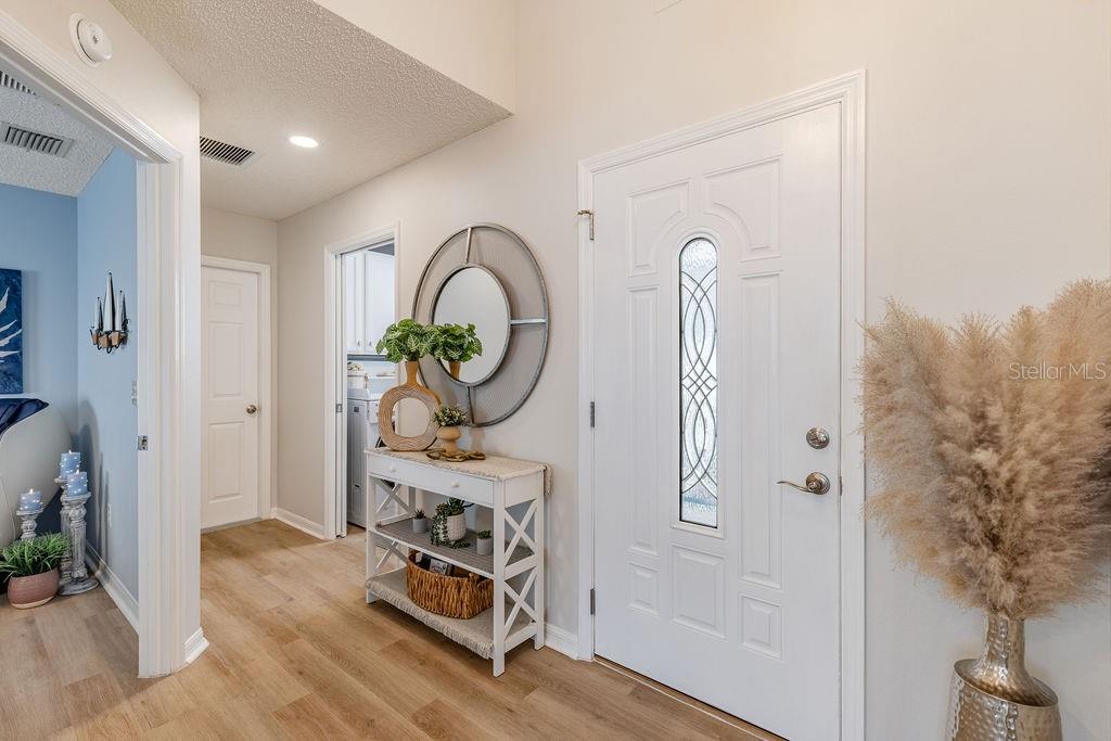 An entryway features a white front door, a console table with decor, and wood-look flooring — 8975 SE 168TH TAILFER STREET, THE VILLAGES, FL