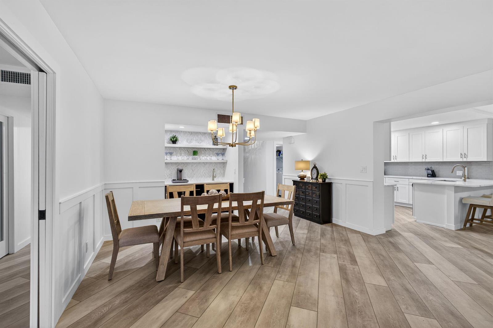A dining room with a wooden table, chandelier, and adjacent kitchen with white cabinetry — 19149 SE Sea Turtle Court # 105, Jupiter FL 33469, JUPITER, FL