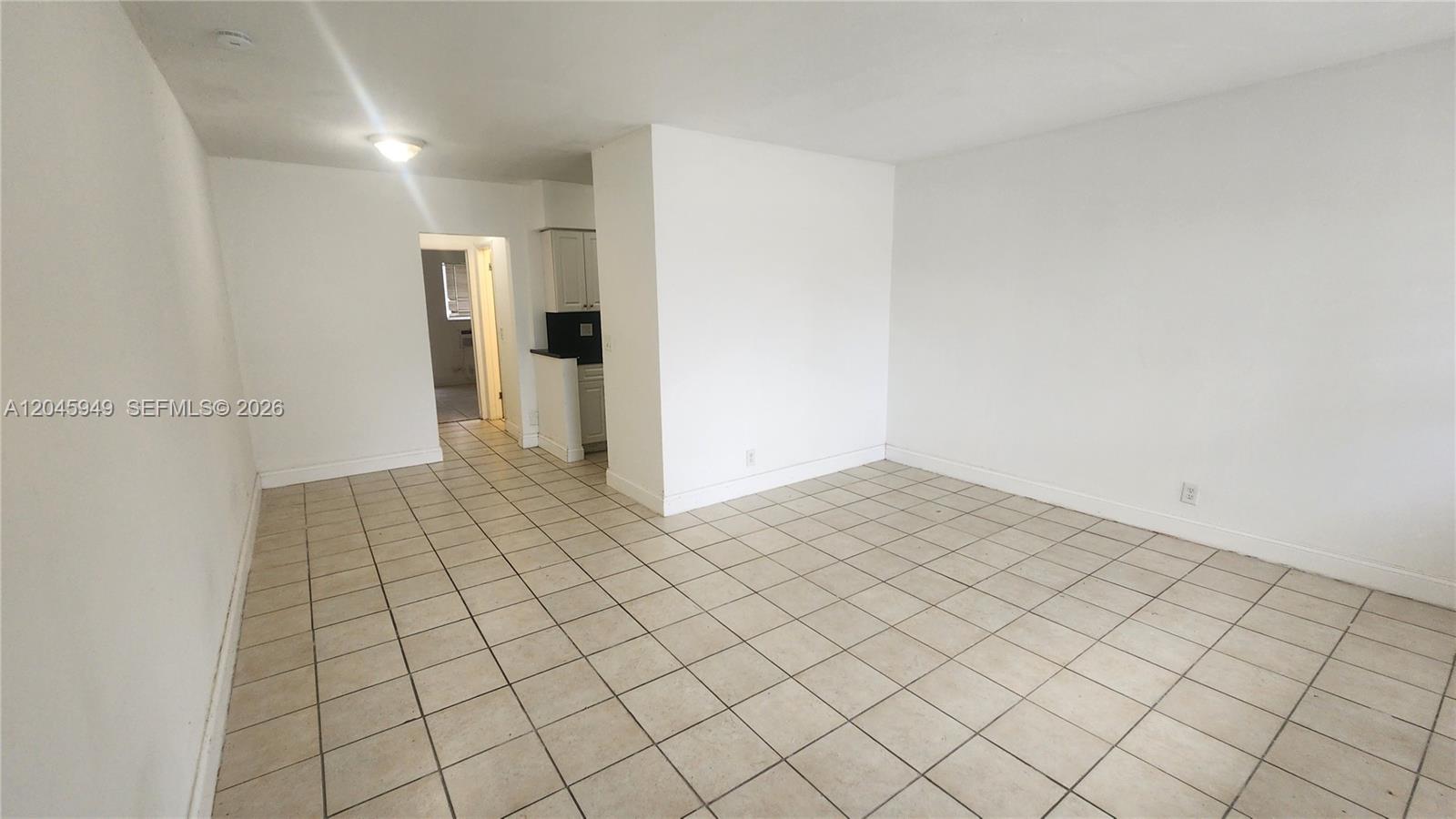An empty room features white walls, a tiled floor, and a doorway leading to a kitchen — 280 SW 11th Ave # 5, Hallandale Beach FL 33009, HALLANDALE BEACH, FL