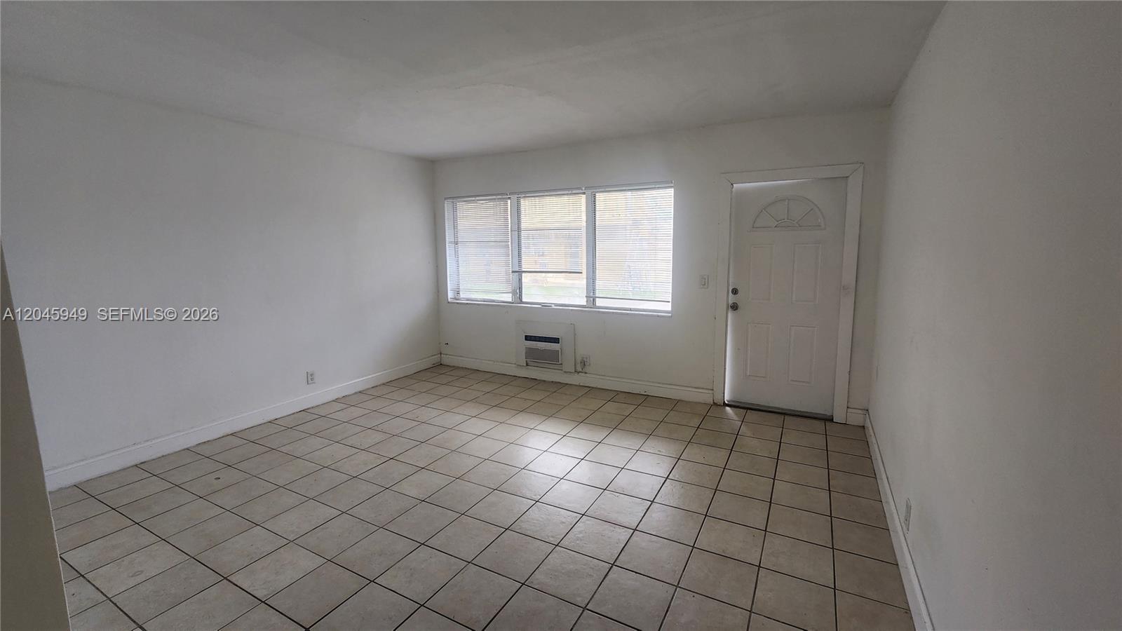 An empty room features white walls, tiled flooring, a window with blinds, and a door — 280 SW 11th Ave # 5, Hallandale Beach FL 33009, HALLANDALE BEACH, FL