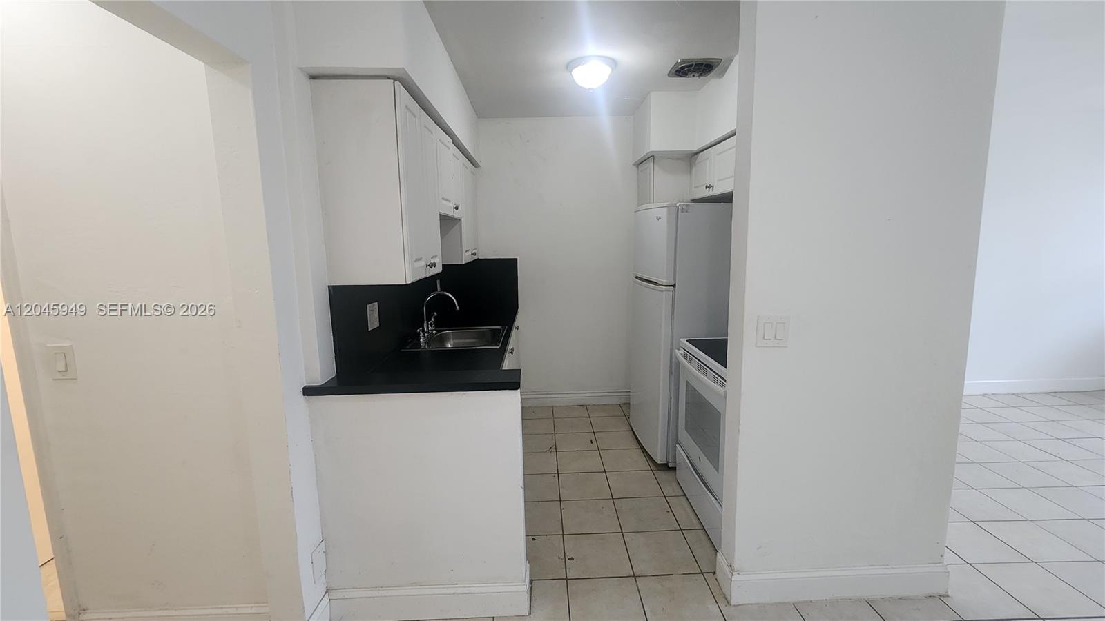 A small galley kitchen features white cabinets, black countertops, and white appliances — 280 SW 11th Ave # 5, Hallandale Beach FL 33009, HALLANDALE BEACH, FL