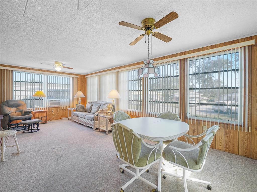 A living and dining area features wood-paneled walls, carpeted floors, and multiple large windows — 27 SADDLEBAG TRAIL S, LAKE WALES, FL