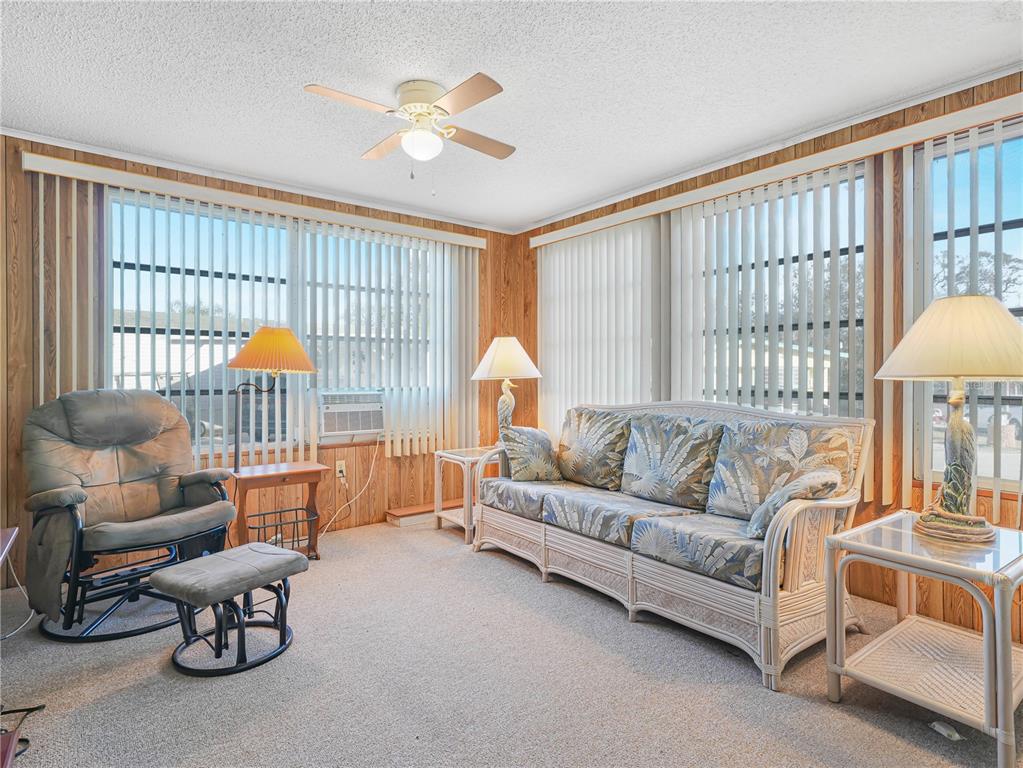 A sunroom features wood-paneled walls, vertical blinds, a ceiling fan, and wicker-style furniture — 27 SADDLEBAG TRAIL S, LAKE WALES, FL