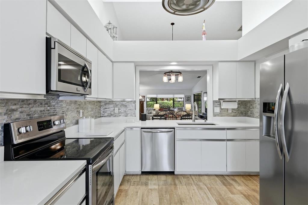 A modern kitchen features white cabinets, stainless steel appliances, and a stone tile backsplash — 2644 MOSS OAK DRIVE UNIT 47, SARASOTA, FL