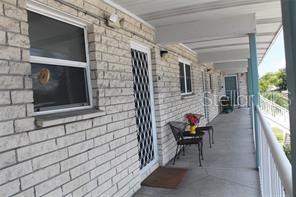 A brick exterior walkway features a covered porch with a metal railing and patio chairs — 5357 81ST STREET N UNIT 24, ST PETERSBURG, FL
