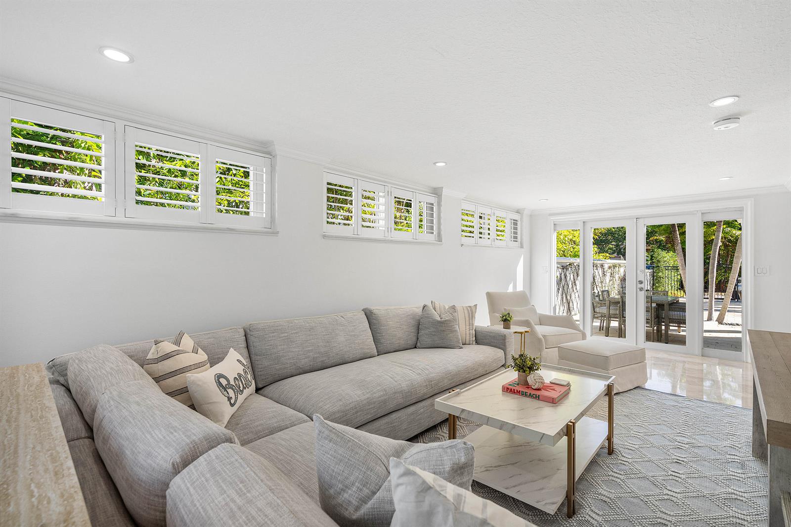 A bright living room features a large gray sectional, marble coffee table, and plantation shutters — 820 Palm Trail, Delray Beach FL 33483, DELRAY BEACH, FL