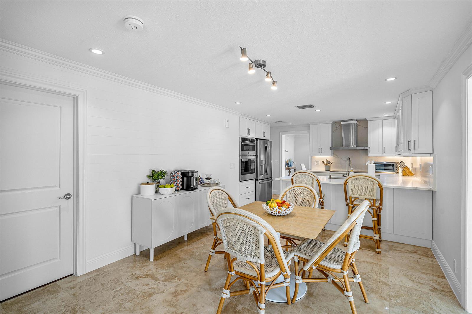 A white kitchen features a dining table, rattan chairs, stainless appliances, and light tile flooring — 820 Palm Trail, Delray Beach FL 33483, DELRAY BEACH, FL