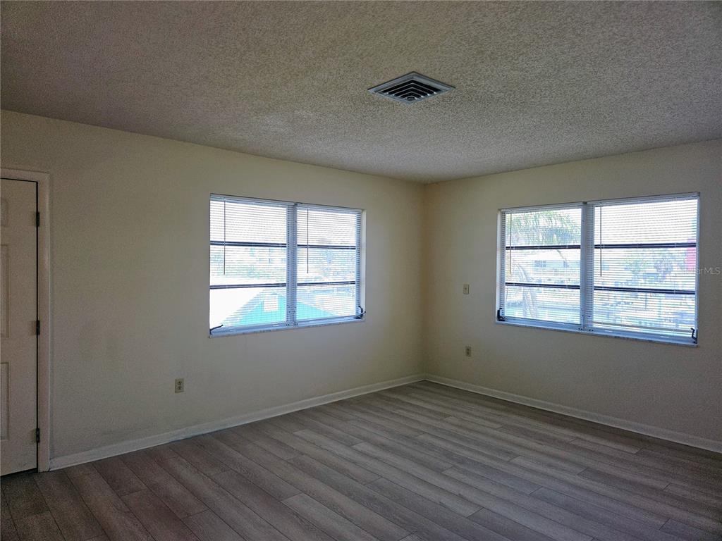An empty room features light-colored wood-look flooring, beige walls, and two windows with blinds — 360 137TH AVENUE CIRCLE UNIT 360, MADEIRA BEACH, FL