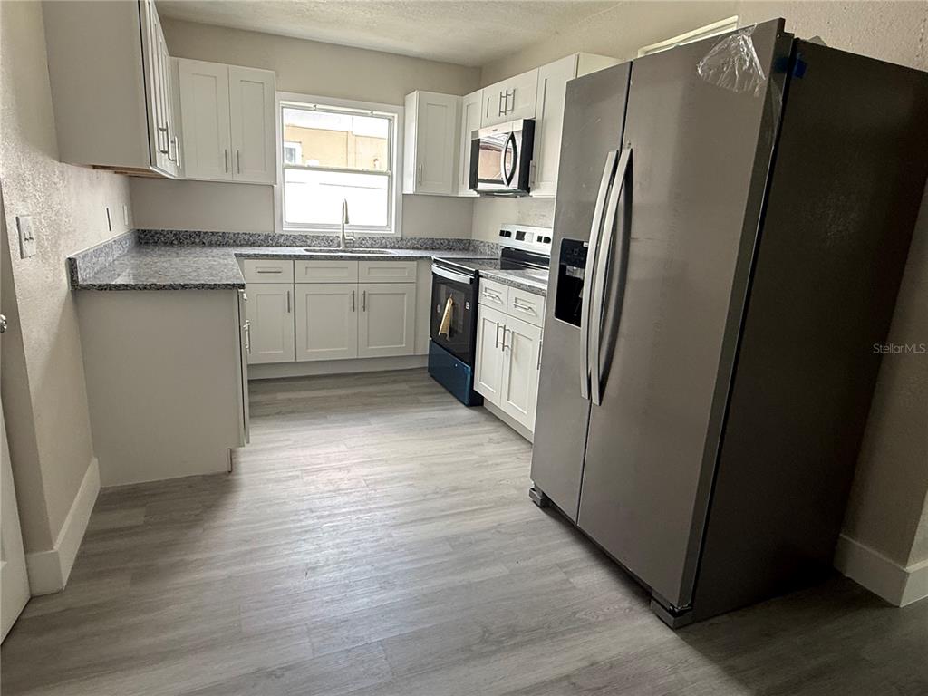 A kitchen features white cabinets, granite countertops, stainless steel appliances, and light wood-look flooring — 5612 LARIMER DRIVE, TAMPA, FL