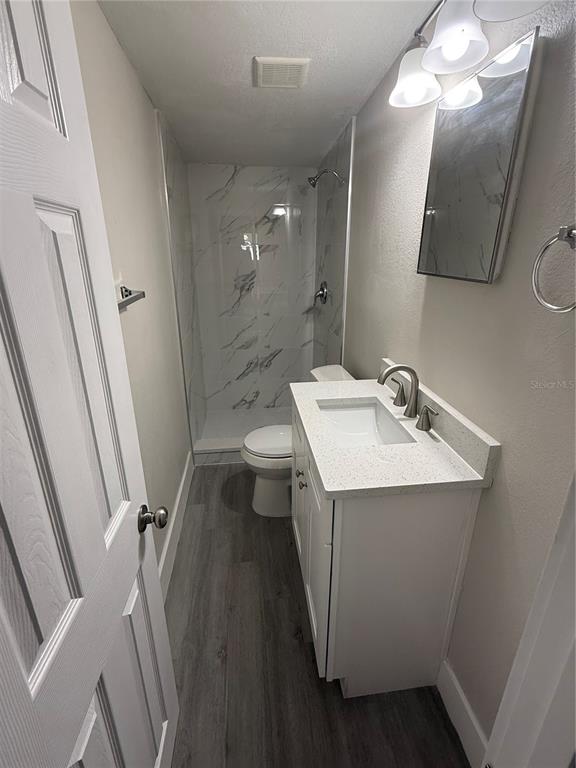 A small bathroom features a white vanity, a toilet, and a marble-tiled walk-in shower — 5612 LARIMER DRIVE, TAMPA, FL