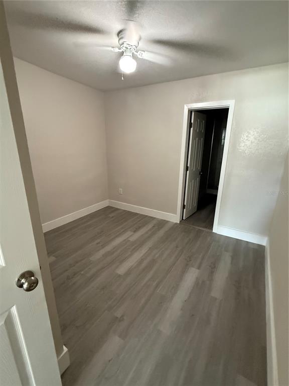 A bedroom with light gray walls, wood-look flooring, a ceiling fan, and a doorway — 5612 LARIMER DRIVE, TAMPA, FL