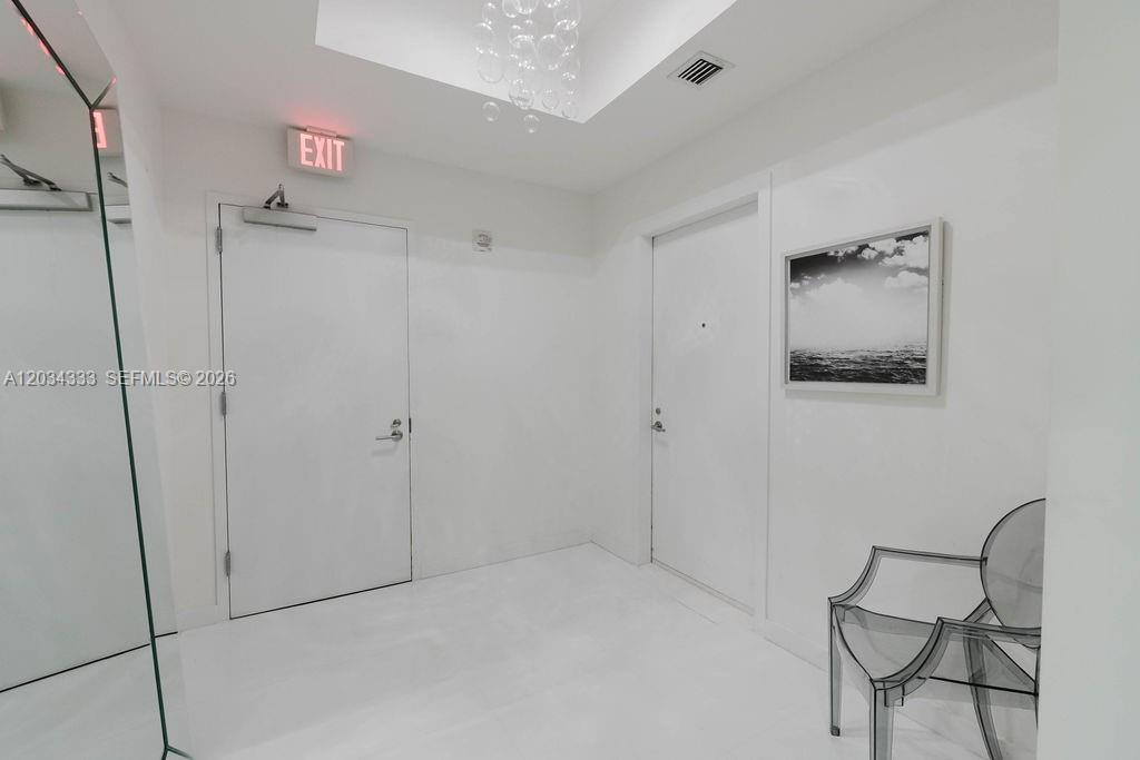 A minimalist white entryway features two doors, a modern transparent chair, and a framed print — 851 NE 1st Ave # 2303, Miami FL 33132, MIAMI, FL