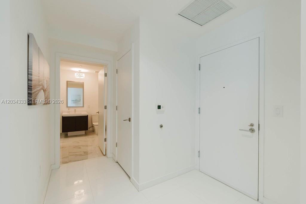 A white hallway leads to a bathroom with a vanity and tiled floors — 851 NE 1st Ave # 2303, Miami FL 33132, MIAMI, FL