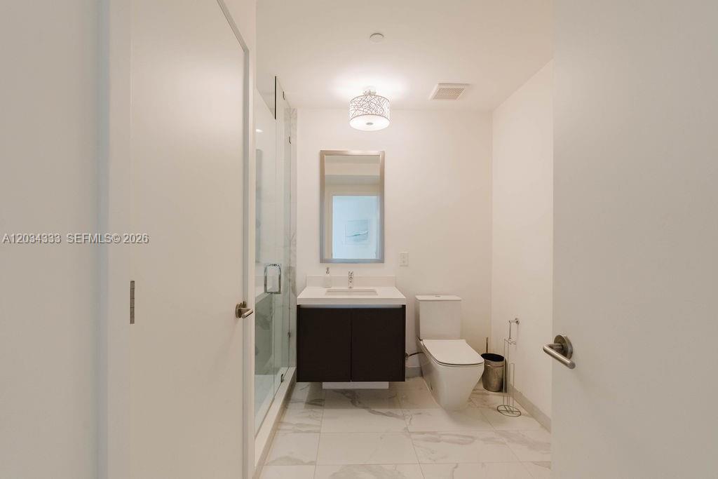 A modern bathroom features a glass-enclosed shower, a dark vanity, and white marble-style flooring — 851 NE 1st Ave # 2303, Miami FL 33132, MIAMI, FL