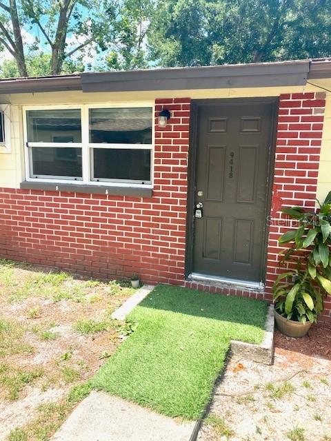 A brick exterior wall features a dark brown front door and a white-framed window — 9420 GREYSTONE ROAD, THONOTOSASSA, FL