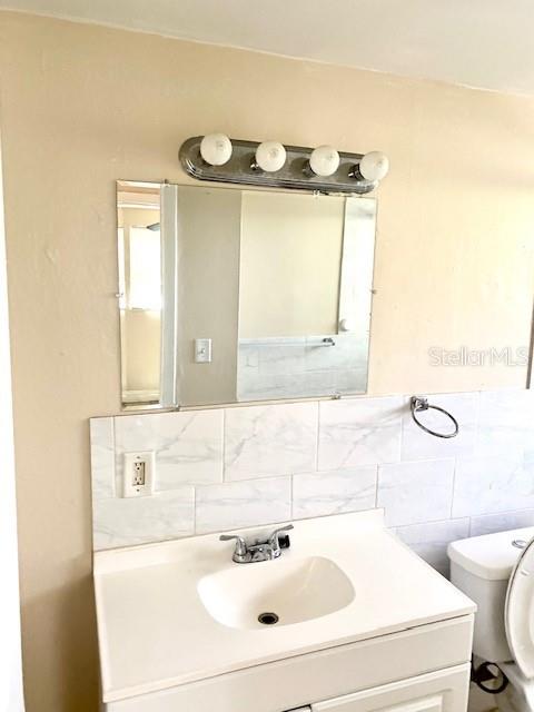 A bathroom vanity features a white sink, marble-look tile backsplash, and a four-bulb light fixture — 9420 GREYSTONE ROAD, THONOTOSASSA, FL