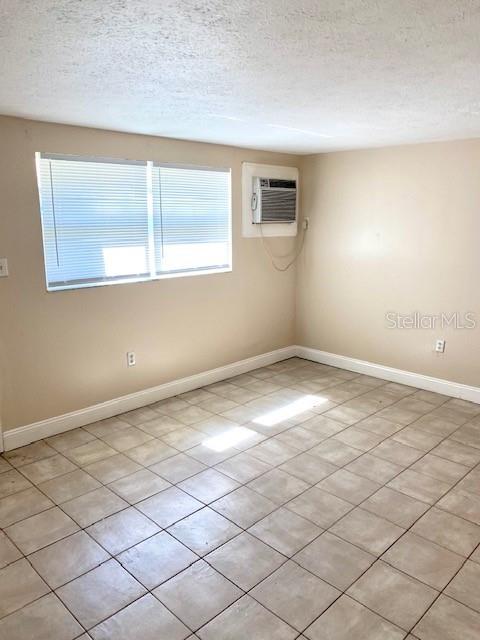 An empty room features light-colored tile flooring, a window with blinds, and a wall-mounted air conditioner — 9420 GREYSTONE ROAD, THONOTOSASSA, FL