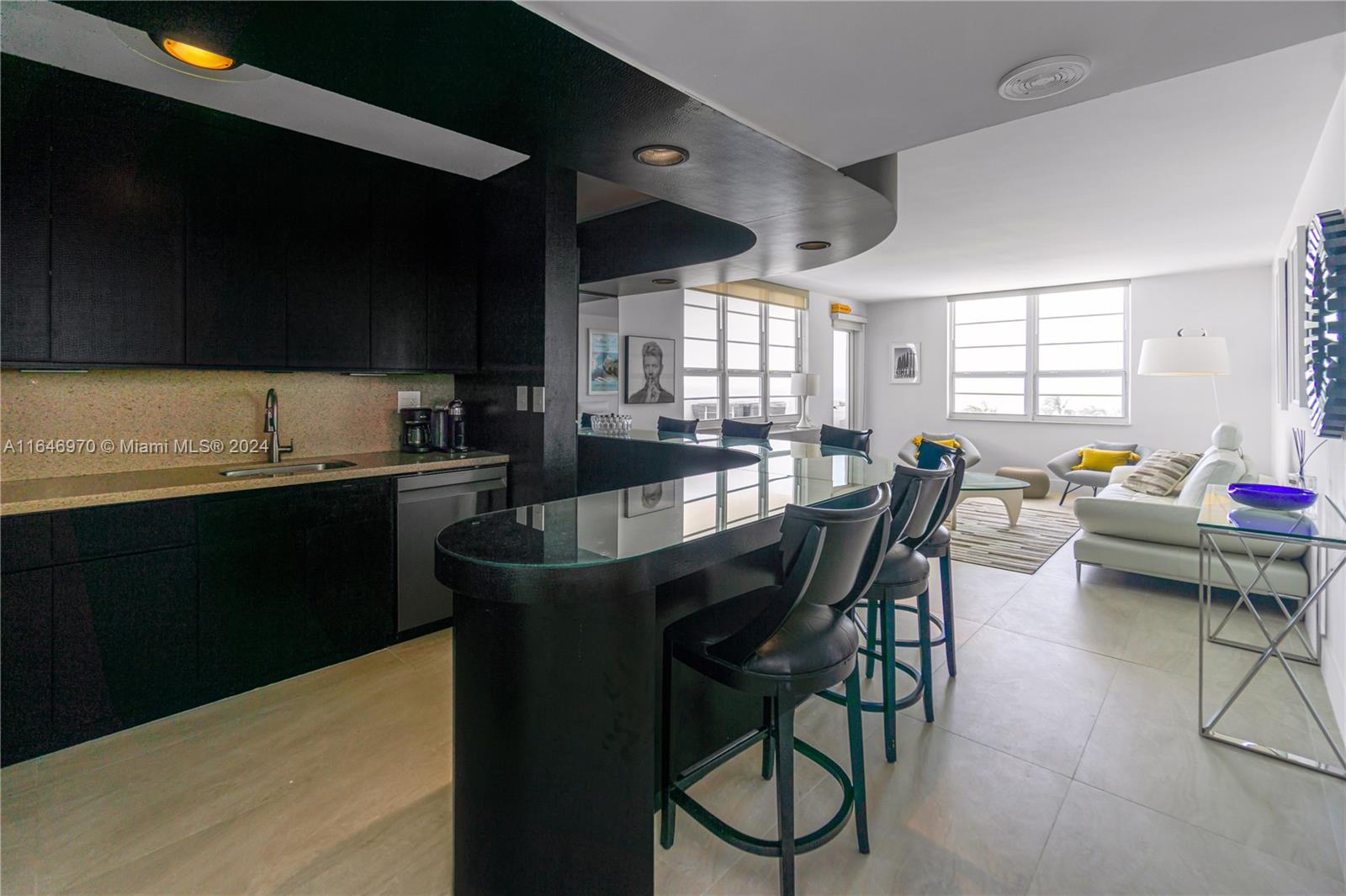 A modern kitchen with black cabinetry and a glass-topped breakfast bar overlooks a living area — 100 Lincoln Rd # 548, Miami Beach FL 33139, MIAMI BEACH, FL